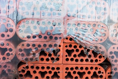 Stack of new silicate bricks with rounded edges in misted torn polyethylene. Closeup.