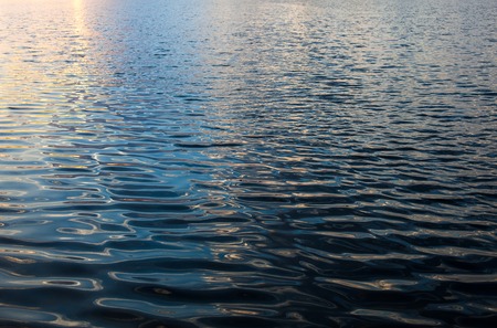 Water surface with ripples and sunrays reflectionsの写真素材