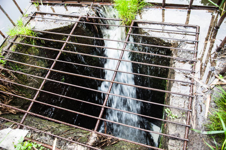 Water flowing into the spillway with metal grate on the dam. Close up.の写真素材