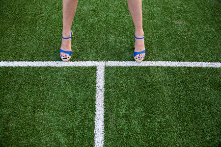 Woman legs in high heel sandals on the soccer field near the white line
