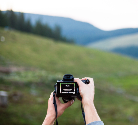 Hands holding the digital photo camera. Looking at the camera settings on the screen.の写真素材