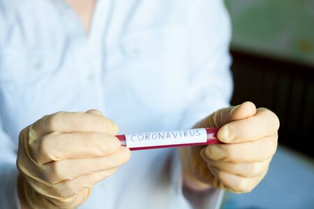 Hands in medical gloves holding blood test tube with results for Coronavirus (Covid-19) infection. Coronavirus disease outbreak.の写真素材