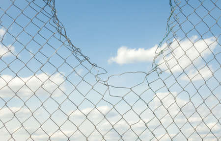 Broken metal mesh fence against the blue sky.の写真素材