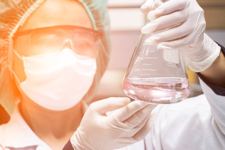 Scientist is lookiing at erlenmeyer flask to observe the chemical reaction
