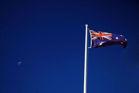 waving australian flag on a post, blue sky, moonの写真素材