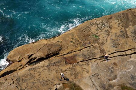 rocky ocean coastline, two fisherman and angling rodsの写真素材
