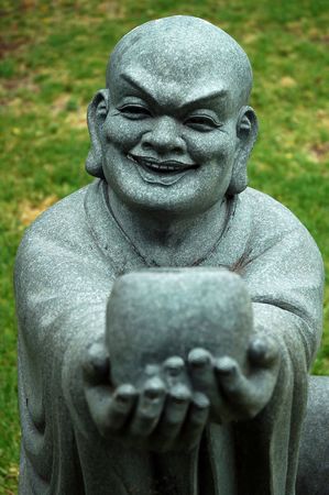 stone buddha sculpture offering a cup and smiling, grass in backgroundの写真素材