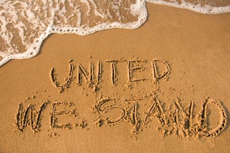 UNITED WE STAND sign written on a beach, water approachingの写真素材