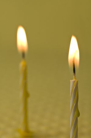 two small burning candles on yellow background, shallow depth of fieldの写真素材