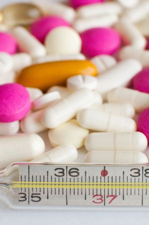 several different pills behind a medical thermometer