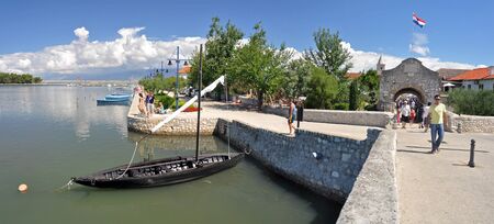 panorama photo of entrance to old town of Nin, small ancient fishing boat anchoring near the entrance bridgeのeditorial素材