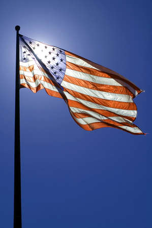 waving american flag, clear blue sky, sun is directly behind the flagの写真素材