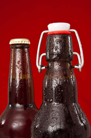 wet brown beer bottles in front of a red background.の写真素材
