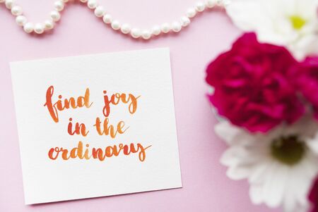 Inspirational quote "Find joy in the ordinary" written in calligraphy style with watercolor. Composition on a pink background. Flat layの写真素材