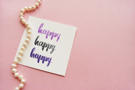 Happy handwritten with watercolor in calligraphy style. Composition on a pink background. Top view.の写真素材