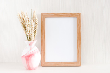 Photo frame mock up, bouquet of dry wheat spikelets in pink vase on a white wooden backgroundの写真素材