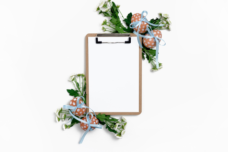Clipboard with Easter eggs tied with blue ribbons and chrysanthemum flowers on white backgroundの写真素材