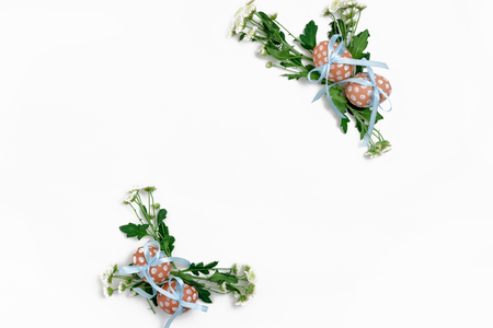 Border frame made of Easter eggs tied with blue ribbons and chrysanthemum flowers on white backgroundの写真素材