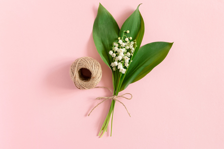 Bouquet of lilies of the valley with green leaves tied with twine on a pink pastel backgroundの写真素材