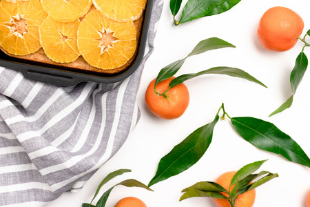 Orange-mandarin pie in baking dish on a striped linen towel. Mandarins on a white backgroundの写真素材