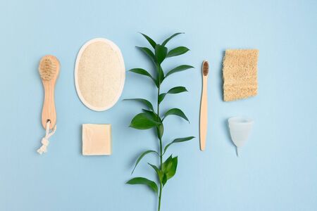Green leaves and zero waste accessories for personal hygiene on blue pastel background.