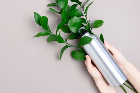 Hands hold metal bottle. Zero waste concept with bouquer of green leaves on gray background.の写真素材