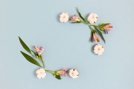 Square frame made of alstroemeria flowers, cotton and green leaves on a blue pastel background. Holiday floral composition.の写真素材