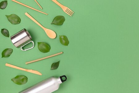 Bamboo cutlery set, metal bottle and mug on a green pastel background. Plastic free concept with copy space.の写真素材