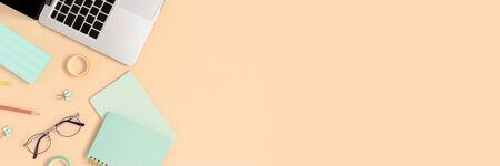 Top view of laptop, glasses and stationery on a yellow pastel background. Workspace concept banner...