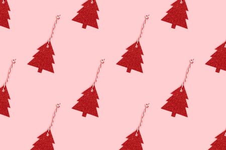 Pattern made of red glittering New Year decorations in a fir-tree shape on a pink pastel background. Festive layout.の写真素材