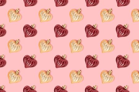 Pattern made of New Year decorations in heart shape on a pink pastel background. Creative festive...