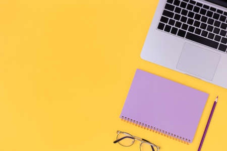 Top view of laptop, glasses and notepad on a bright yellow background. Student workspace concept with copy space.の写真素材