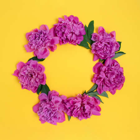 Wreath made of peonies flowers and green leaves on a yellow background. Border frame with copy space.の写真素材