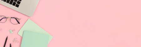 Layout of laptop and stationery on a pink pastel background. Banner with place for text.