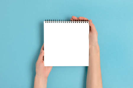 Female hands hold clean notepad. Blank copybook mockup on a blue pastel background.の写真素材