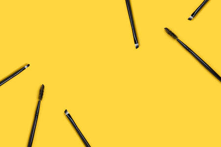 Border frame made of makeup brushes on a yellow background. Beauty composition with place for text.