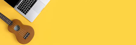 Top view of laptop and ukulele on a bright yellow background with place for text. E-learning the...