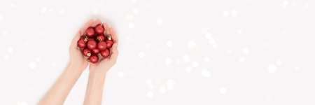 Women hands hold red Christmas balls on a gray background. Glowing festive banner with copy space.の写真素材