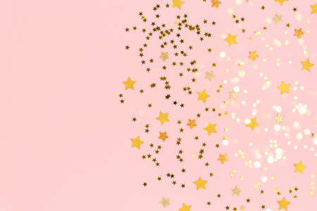 Gold stars confetti scattered on a pink pastel background. Holidays colorful composition with copy space.の写真素材