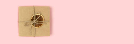 Banner with gift box tied with twine on a pink pastel background. Plastic free concept with place for text.の写真素材