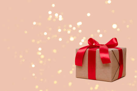 Gift box tied with red ribbon on a beige background with copy space. Festive composition with shiny...
