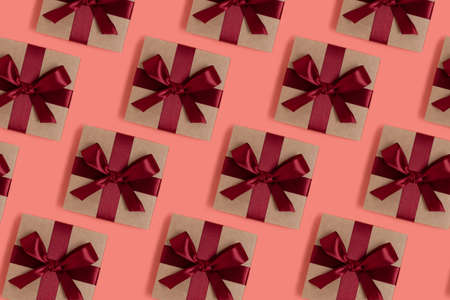 Repetitive pattern made of gift boxes tied with red ribbons on a coral background. Festive concept.