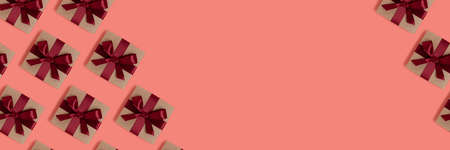 Pattern made of gift boxes tied with red ribbons on a coral background with copy space. Holidays...