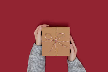 Hands hold gift box tied with rope on a red background. Festive composition with copy space.