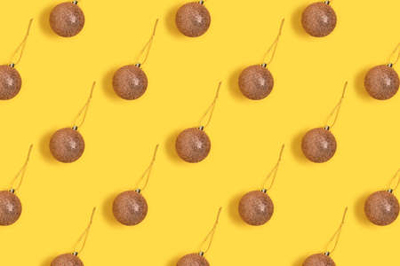 Pattern made of golden shiny Christmas balls on a yellow background. Creative festive concept.