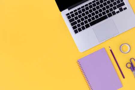 Top view of laptop, glasses, notepad and stationery on a bright yellow background. Student workspace concept with copy space.の写真素材