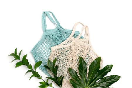 Green leaves and reusable shopping bags on white background