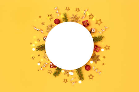 Round paper card mockup with frame made of Christmas toys, confetti and spruce branches. Festive template on a yellow background.の写真素材