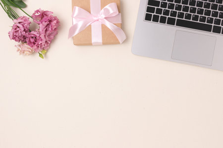 Laptop, bouquet of flowers and gift box with tied bow on a beige background. Copy spaceの写真素材