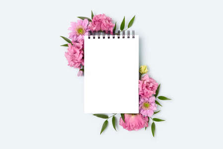 Floral frame made of eustoma flower and empty notepad mockup on a blue pastel background. Spring...